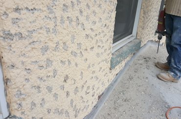 Old painted stucco is chipped using a chipping hammer.